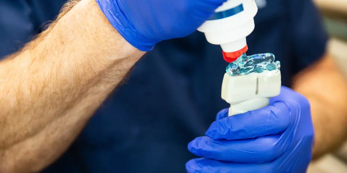 A person wearing blue nitrile gloves is applying a thick, transparent blue